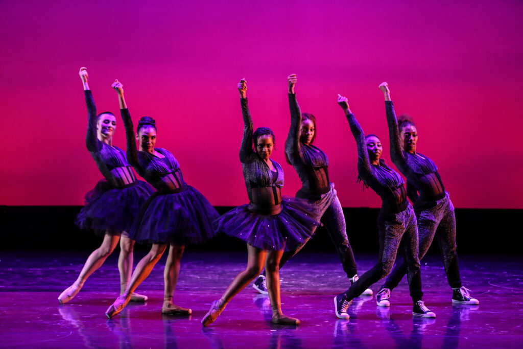 dancers posing on stage in front of a pink background.