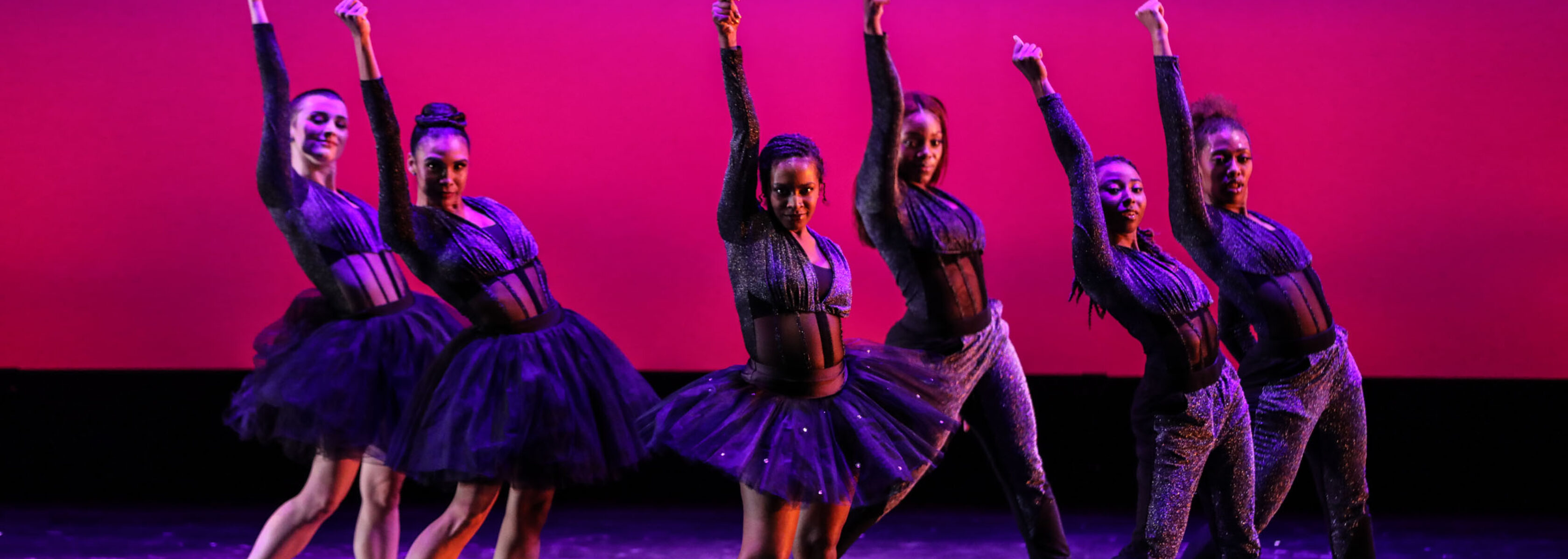 dancers posing on stage in front of a pink background.
