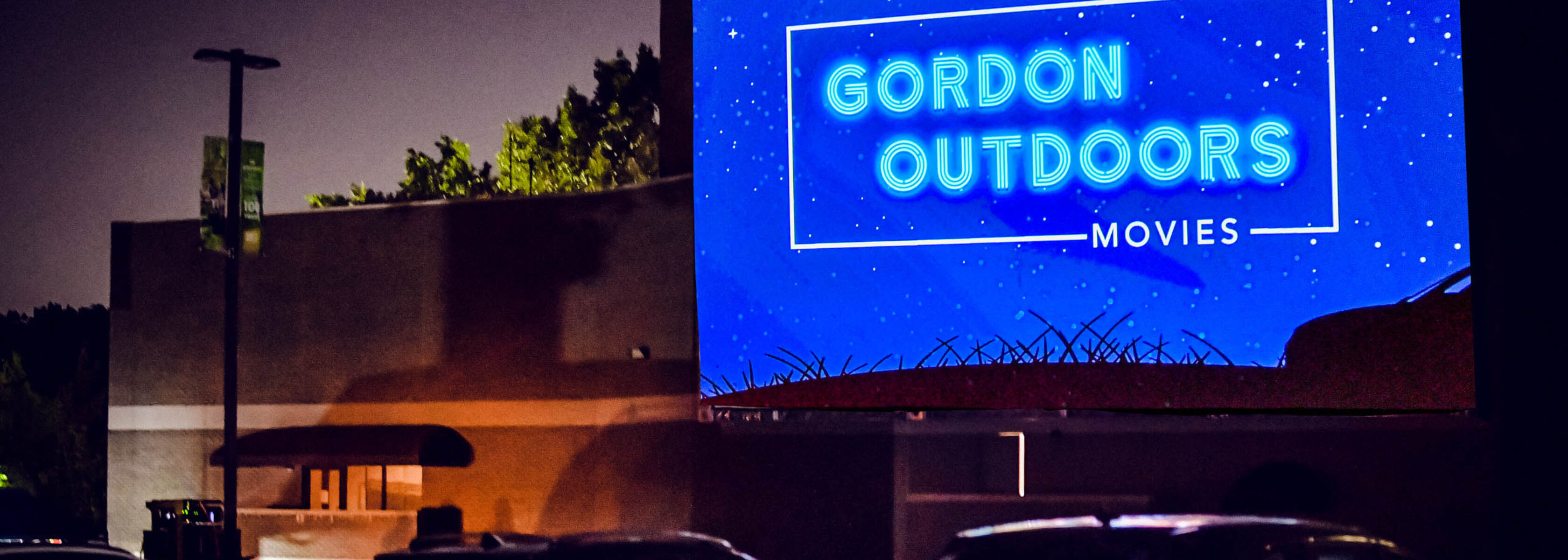 Outdoor movie screen that says Gordon Outdoors with cars in front.