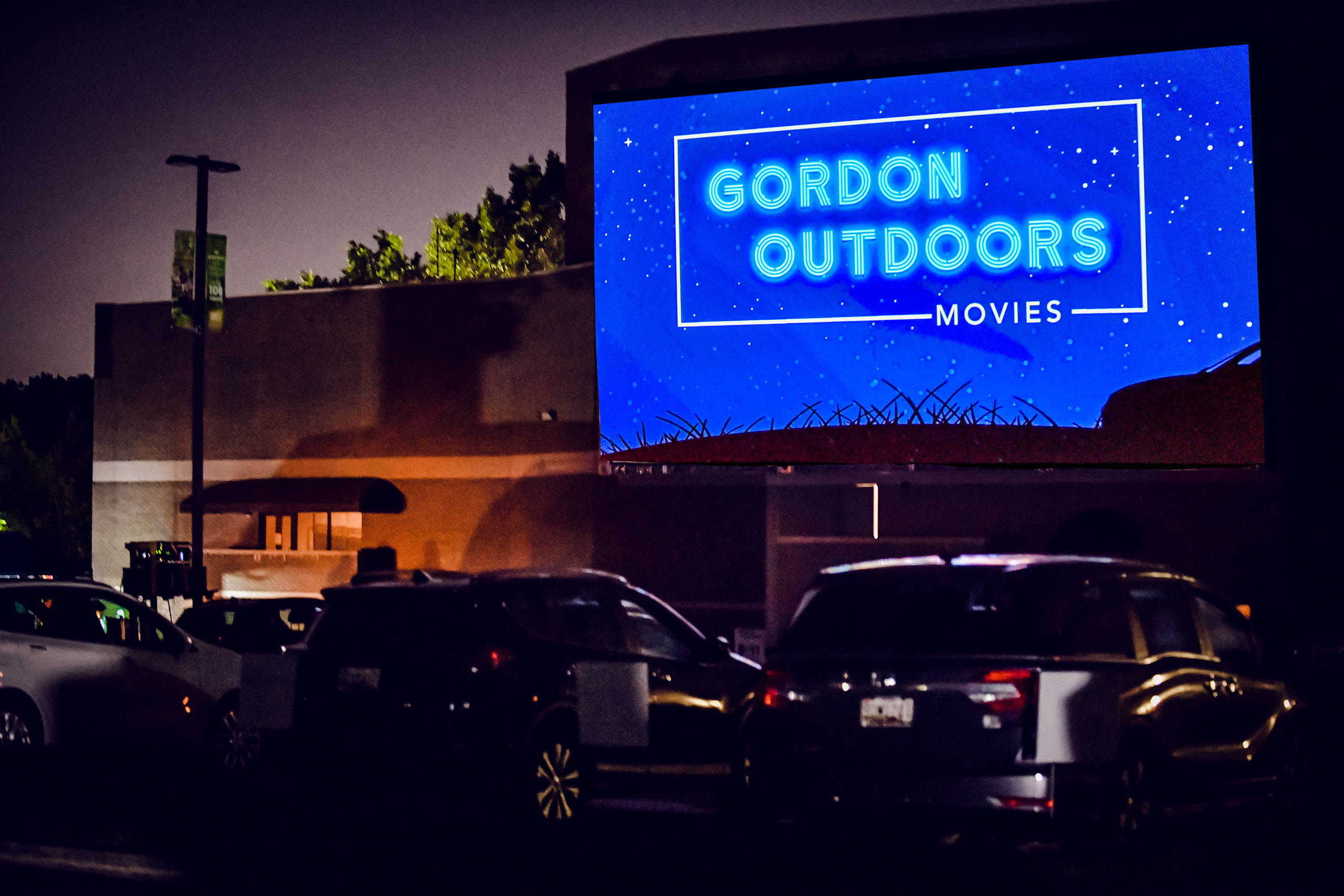 Outdoor movie screen that says Gordon Outdoors with cars in front.